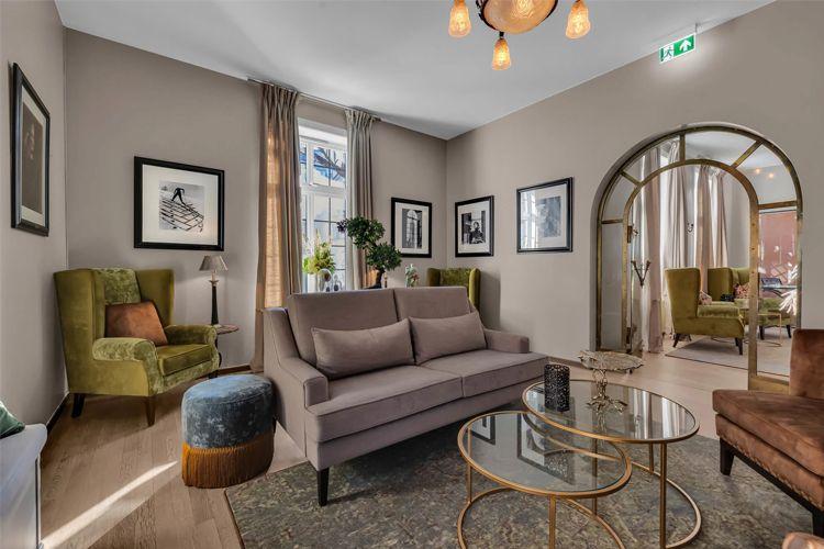 Stue med moderne møbler, inkludert en grå sofa, grønne stoler og dekorative bilder på veggene.