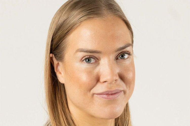 Ung kvinne med langt, lyst hår og naturlig sminke, smilende mot kameraet med en lys bakgrunn.