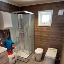 Moderne bad med dusj, toalett og vaskemaskin, samt brune vegger og grå fliser på gulvet.