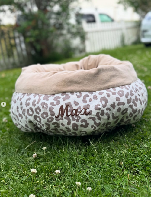 En myk kattekurv med leopardmønster og navnet "Moox" brodert, plassert på grønt gress.