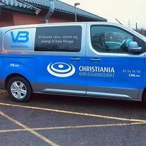 En varebil med VB-logo og Christiania Rørleggerbedrift på siden, parkert utenfor en bygning.