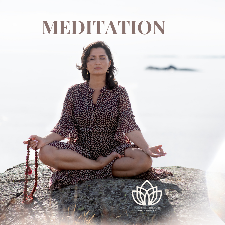 Kvinne med mørkt hår sitter i meditasjonsstilling på en stein ved havet, med fokusert uttrykk og perlekjede.