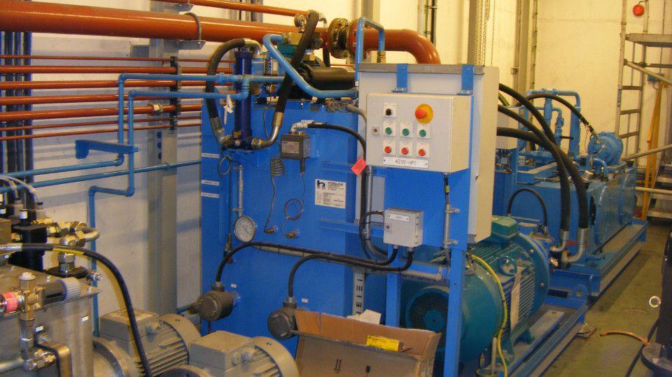 Blå pumper og rørledninger i en industriell setting med kontrollpanel og elektriske komponenter.