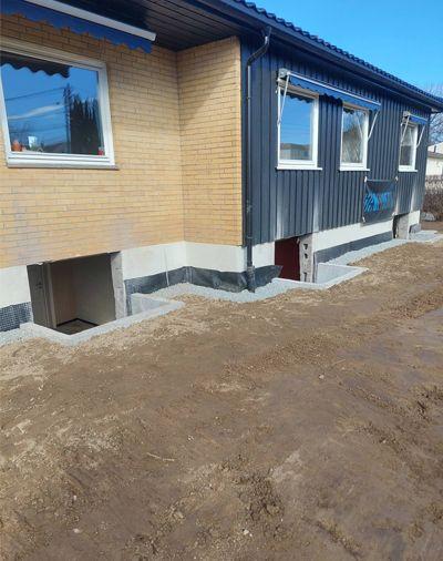 Nybygd hus med murvegg og vinduer, samt gruslagt område rundt fundamentet.