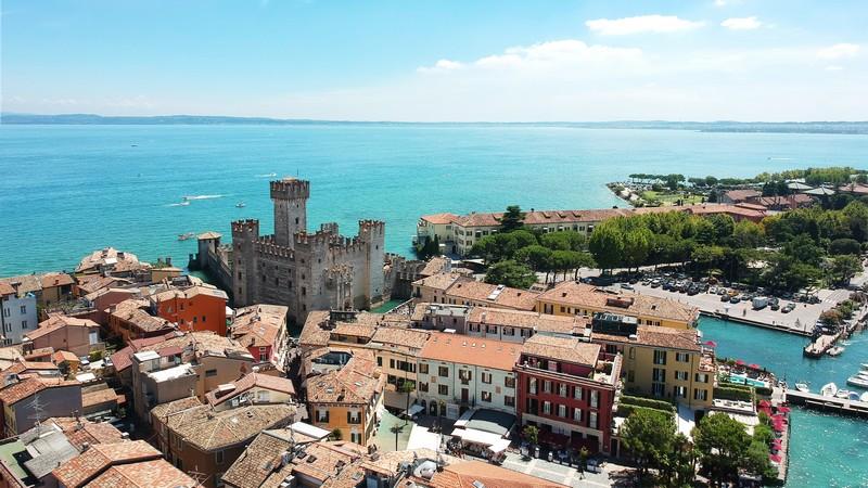 Utsikt over Sirmione med slottet, fargerike bygninger og innsjøen Garda i bakgrunnen.