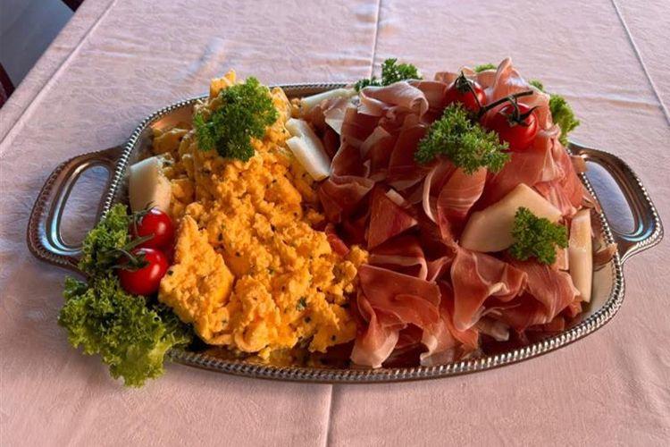 En sølvfat med spekeskinke, eggerøre, poteter, cherrytomater og persille.