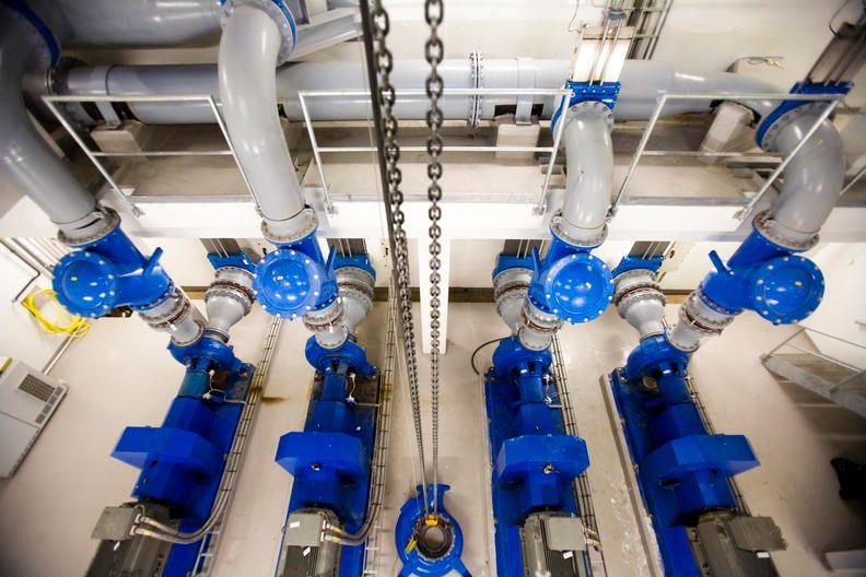 Oversikt over blå rør og pumper i en industriell anlegg, med kjede hengende fra taket.