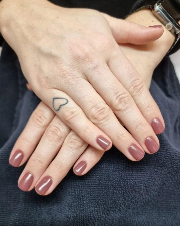 To fingre med velpleide negler i en rosa nyanse, med en liten hjerte-tatovering på den ene hånden.