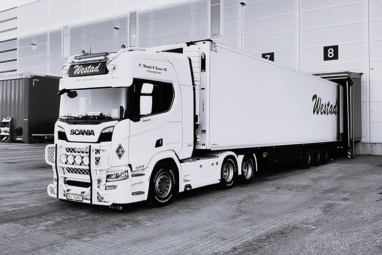 En Scania lastebil med tilhenger står ved en lastebrygge i svart-hvitt.