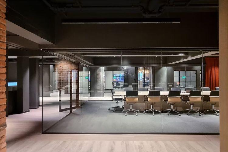 Moderne kontorlandskap med glassvegger, konferanserom og stilige skrivebordstoler.