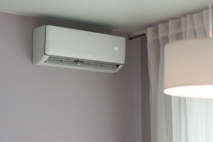 En moderne klimaanlegg montert på veggen i et rom med gardiner og en lampe i bakgrunnen.