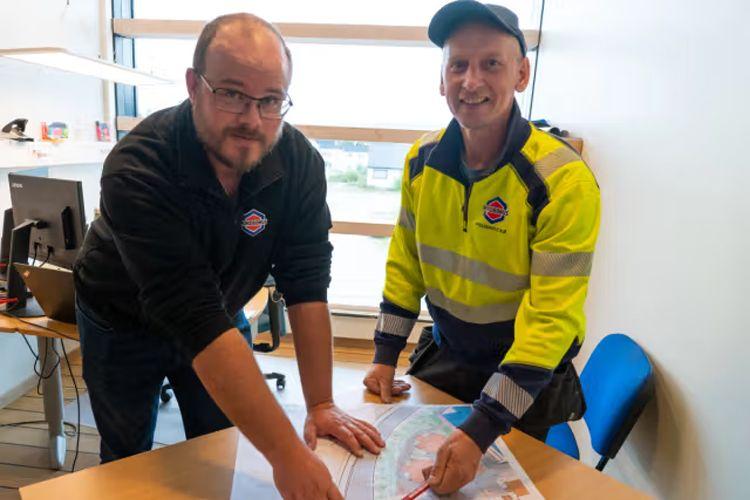 To personer som studerer et kart sammen på et kontor, med en datamaskin i bakgrunnen.