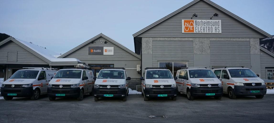Flere servicebiler parkert foran en bygning med grå fasade og skilt i snødekt område.