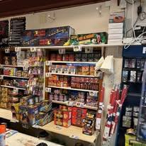 Butikkinnredning med hyller fylt med fyrverkeri og festartikler til salgs.