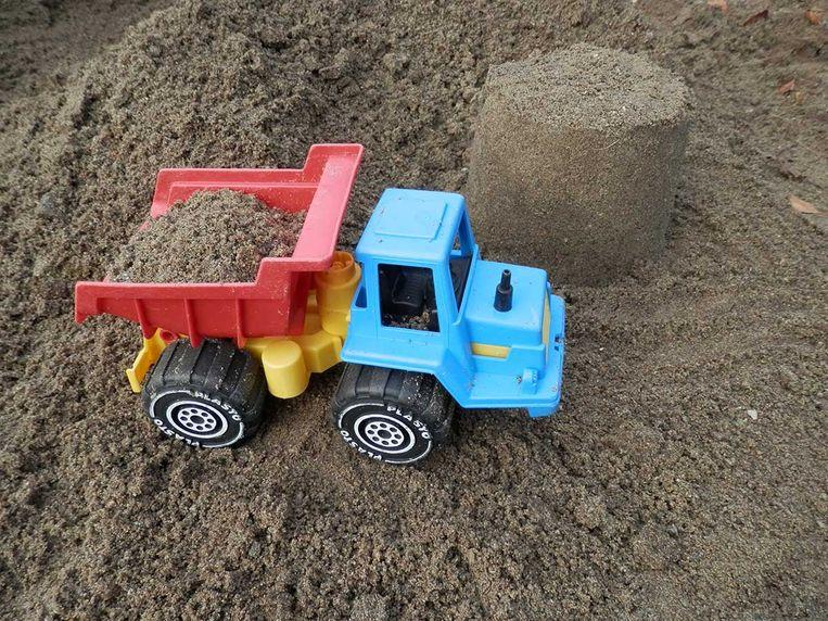 En blå lekebil med rød tilhenger som frakter sand i en sandhaug.