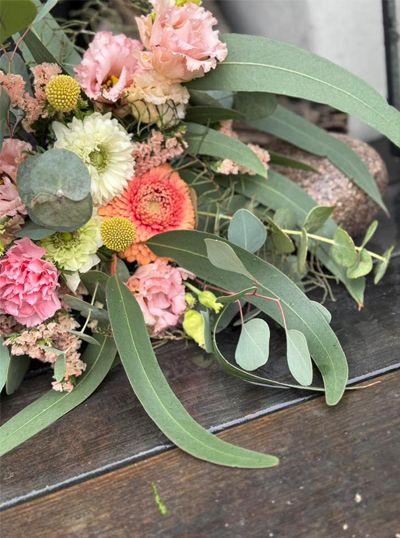 En bukett med rosa og oransje blomster, grønn eucalyptus og tørkede blomster på en treoverflate.
