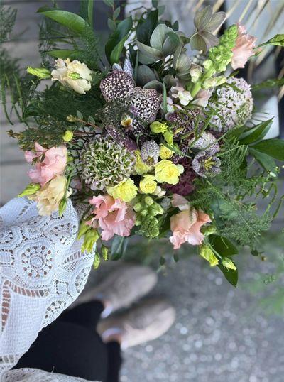 En bukett med fargerike blomster, inkludert roser og grønt, holdt av en person med lys genser og sko.