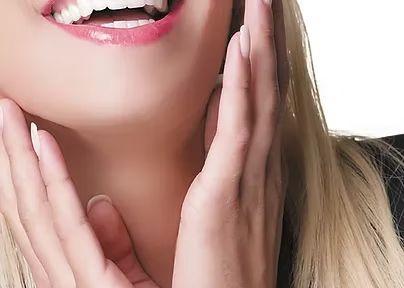 En kvinne med blondt hår smiler bredt og holder hendene på ansiktet sitt.