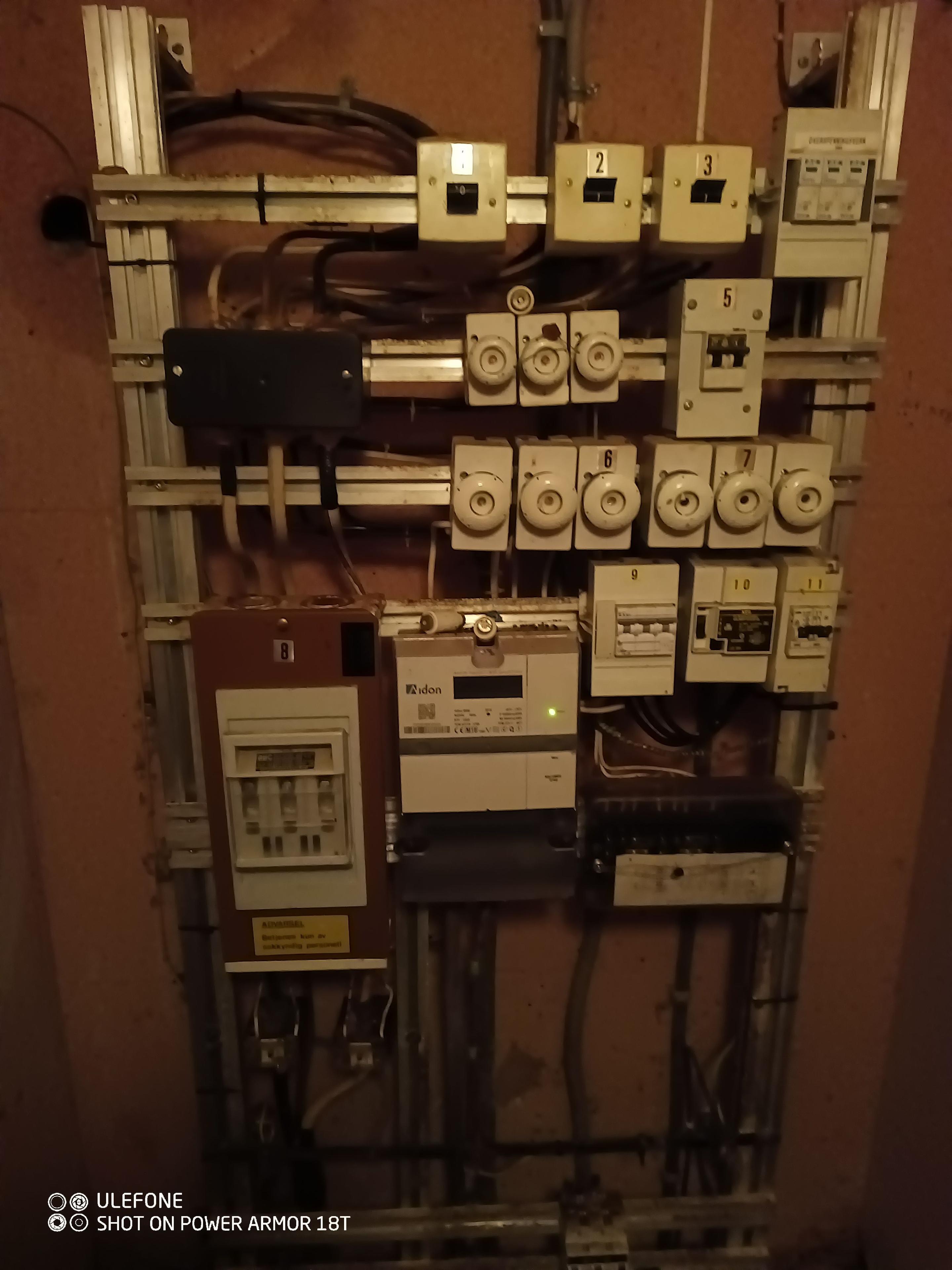 En elektrisk tavle med sikringer, målere og ledninger montert på en vegg.