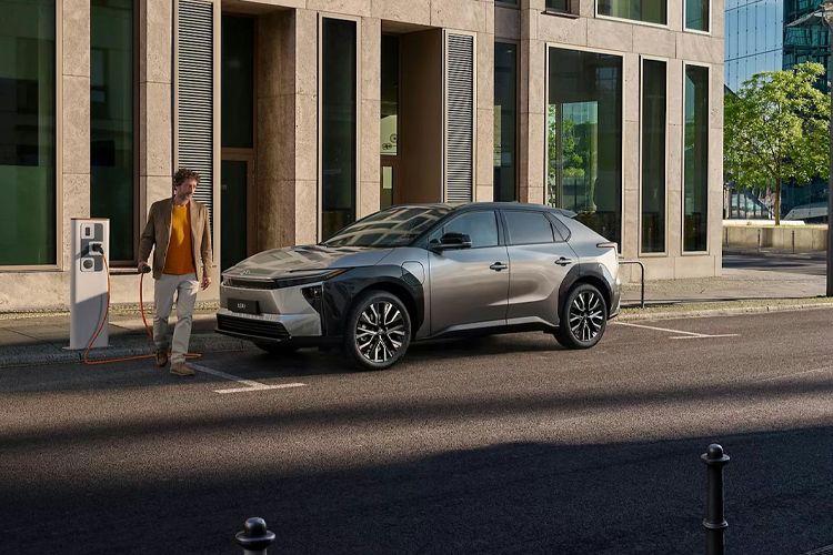 En mann går mot en sølvfarget elbil parkert ved en moderne bygning i byen.