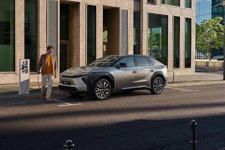 En moderne elbil parkert på gaten foran en moderne bygning, med en person som går mot ladestasjonen.
