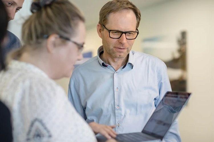 To personer ser på en laptop sammen i et kontormiljø, med fokus på skjermen og samarbeid.