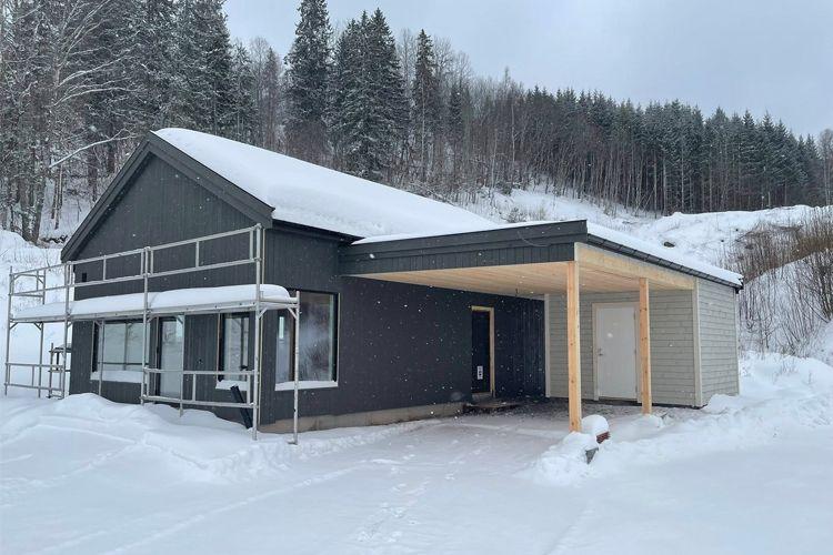 Moderne enebolig med tak i snø, omringet av vinterlandskap og trær i bakgrunnen.