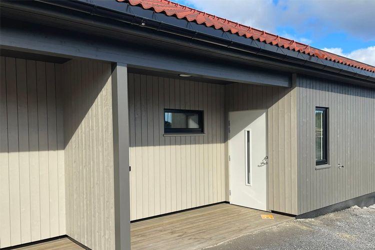 Moderne husfasade med trepanel, vinduer og en inngangsdør, under en blå himmel med skyer.