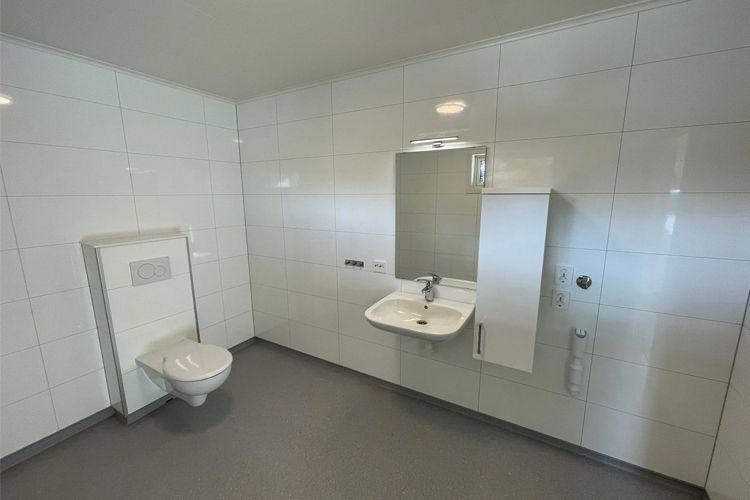 Moderne baderom med hvite fliser, servant, speil og toalett i et lyst rom.