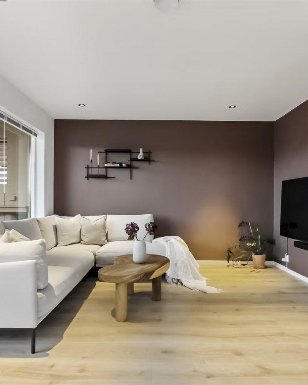 Moderne stue med en hvit sofa, trekaffebord, planter og en brun vegg.