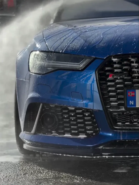 Blå Audi RS7 med vannsprut, fokusert på fronten og grillen, under bilvask.