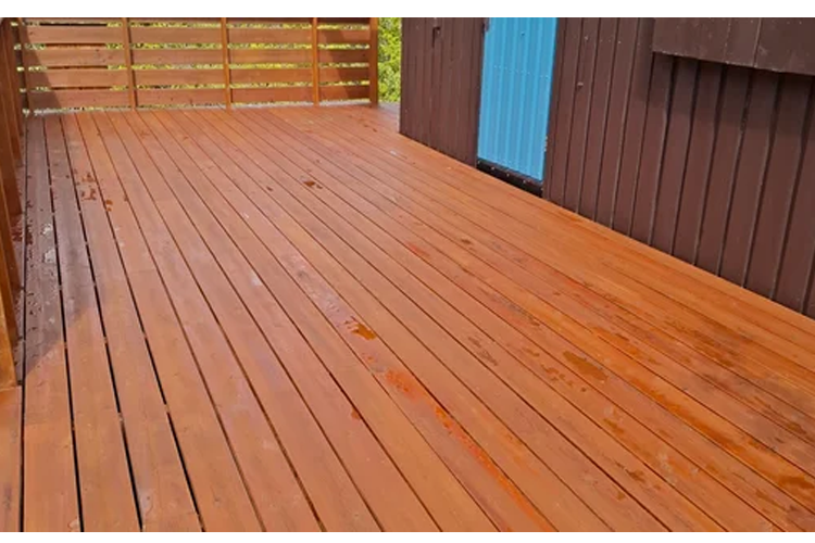Tregulv på en terrasse med brune planker og en vegg i blått og brunt. Det er vått etter regn.