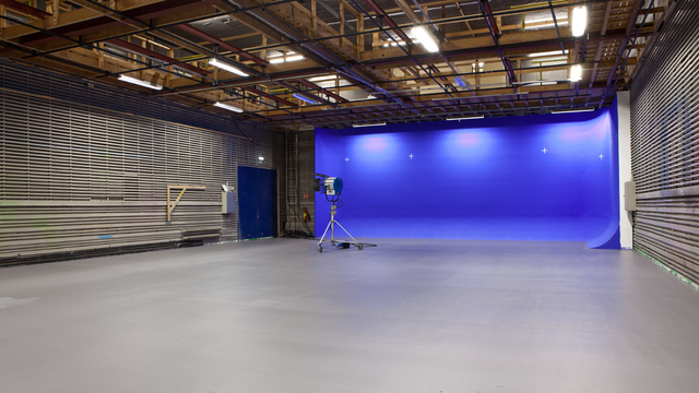 Tom studio med blå bakgrunn, lysutstyr og grått gulv, klart for film- eller fotoproduksjon.