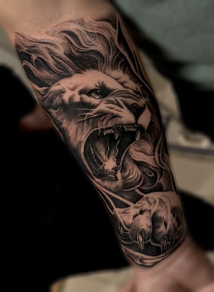 Tatovering av en brølende løve med detaljerte manker og klør på en arm.