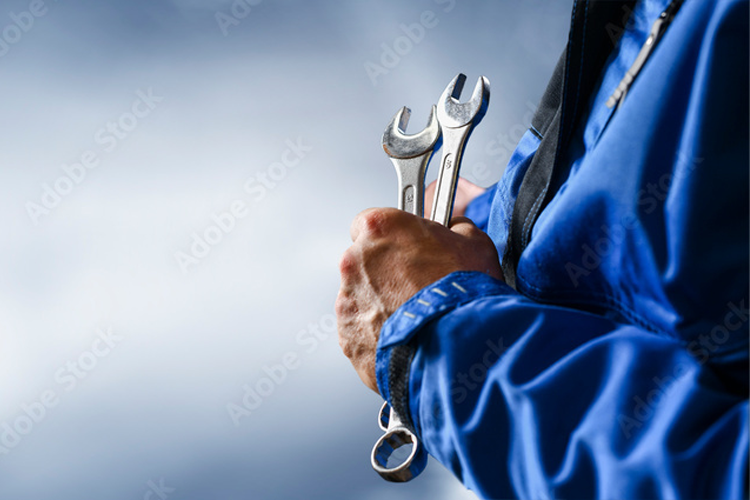 En person holder to verktøy i hånden, med en blå jakke og en skyet bakgrunn.