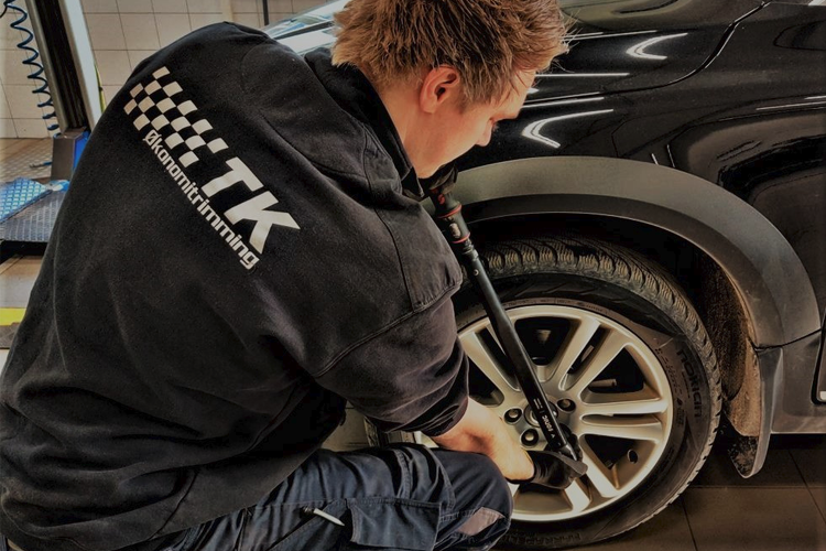 En mekaniker skifter dekk på en bil med en momentnøkkel i et verksted.