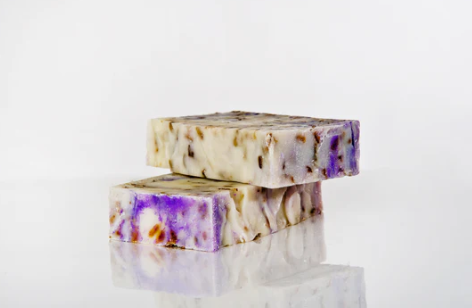 Tofargede såpestykker med lavendel og urter, plassert på en reflekterende overflate.