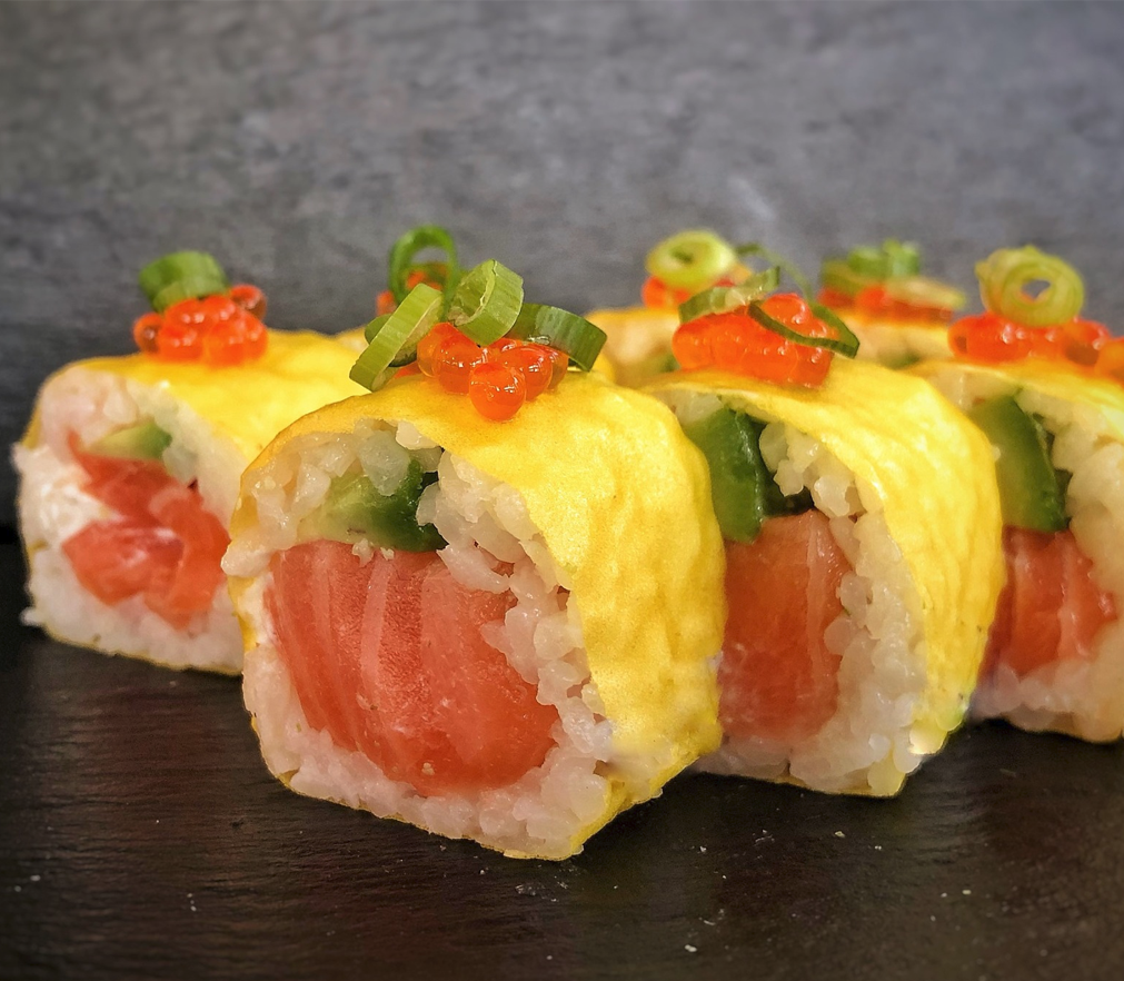 Sushi med laks, avokado og grønne løk, rullet i ris og egg, pyntet med fiskeegg.
