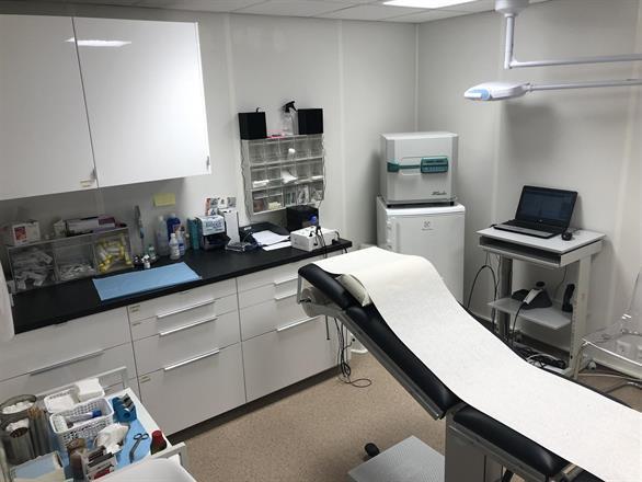 Moderne legekontor med behandlingsbenk, medisinsk utstyr og datamaskin på skrivebordet.