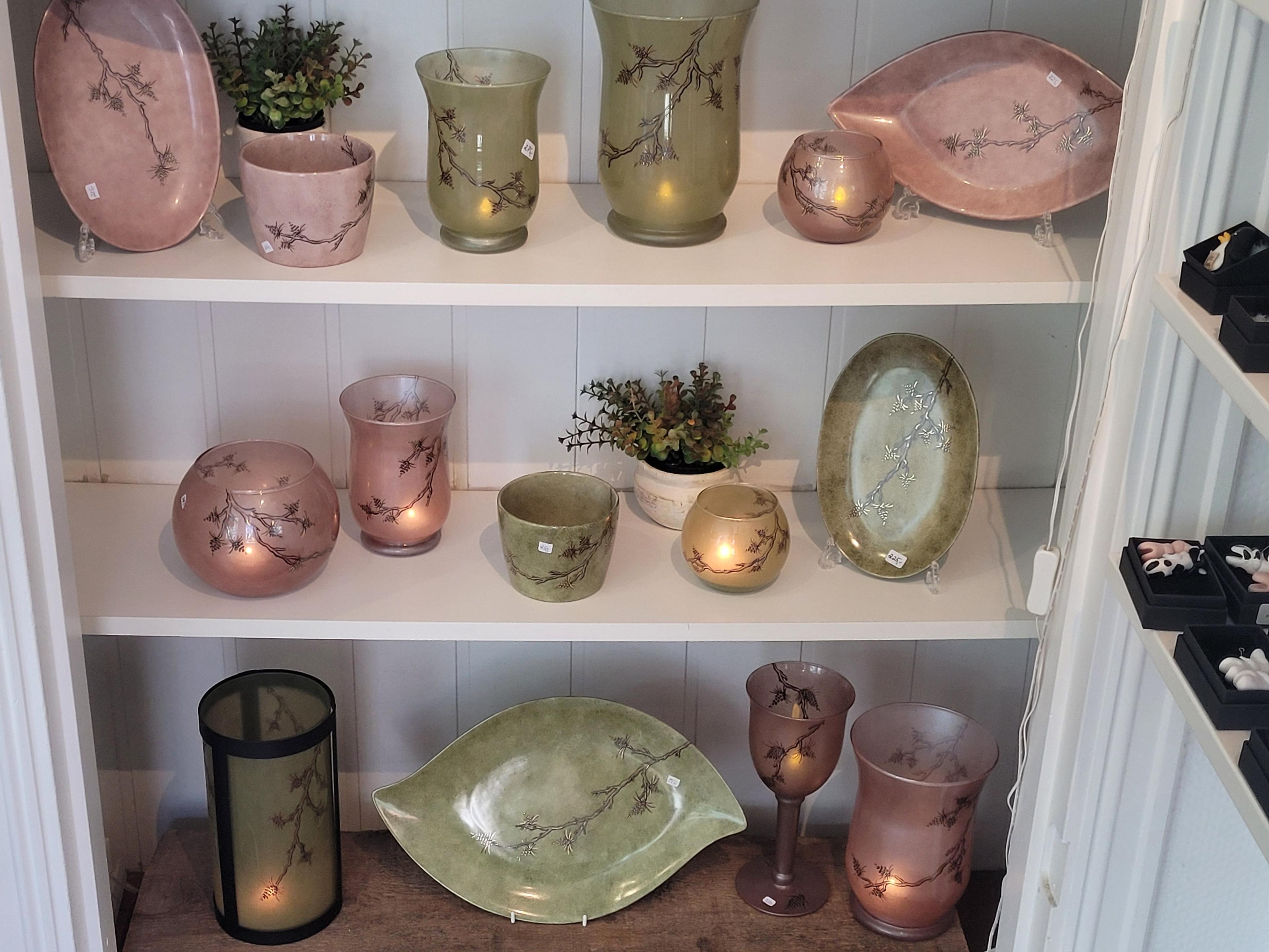 Vitrineskap med dekorative glassvaser, lysestaker og planter i forskjellige farger og former.