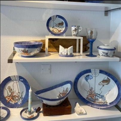 Kreativ servise med blått og hvitt design, inkludert skåler, tallerkener og glass, utstilt på en hylle.