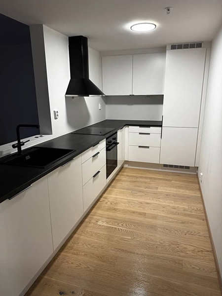 Moderne kjøkken med hvite skap, svart benkeplate og treverk gulv, samt en ventilator over komfyren.