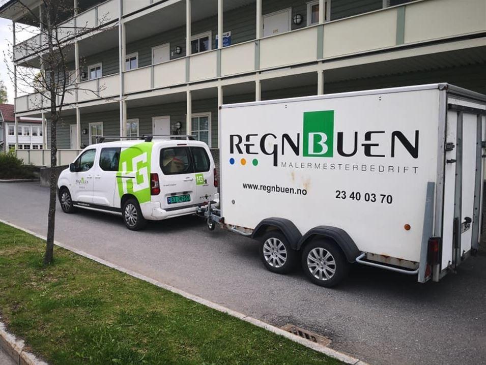 En hvit varebil med logo og en tilhenger parkert foran en bygning.