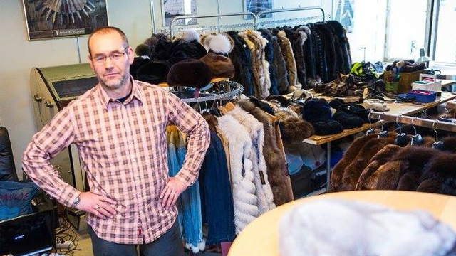 En mann står foran en butikk med pelsjakker og tilbehør, omringet av ulike farger og stiler.