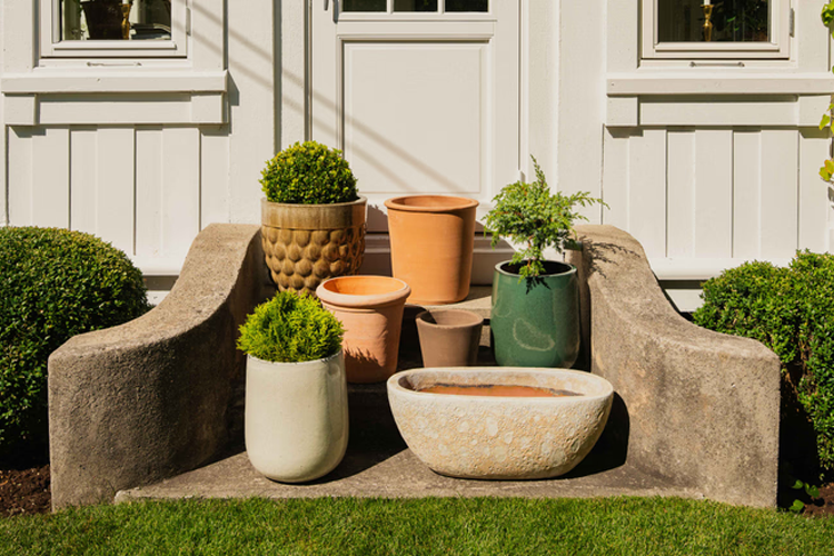 Flere blomsterpotter i forskjellige størrelser og farger plassert på en trapp foran en hvit dør.