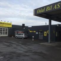 Odal Bil AS med verksted og bilutstilling under tak, grå bygning og gule skilt.