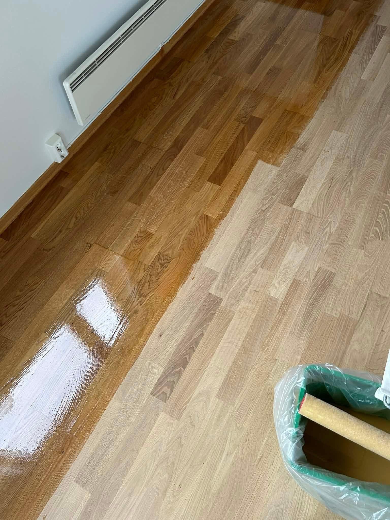 Gulv med ny lakkert overflate, malerulle og bøtte i hjørnet av rommet.