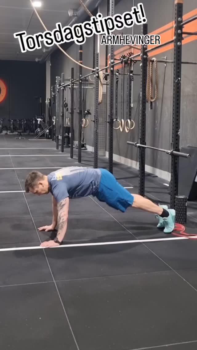 En mann utfører en push-up i et treningsstudio med treningsutstyr i bakgrunnen.