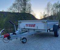 En Tysse tilhenger parkert på grusvei med fjell og trær i bakgrunnen under solnedgang.