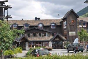Et stort, moderne hotell med tre- og steinfasade, omgitt av grønt landskap og fjell i bakgrunnen.
